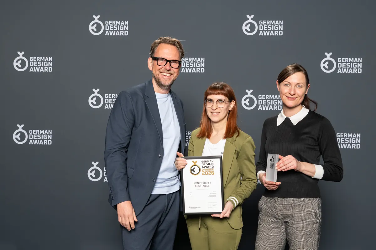 Urkunde und Trophäe des German Design Award werden vor der Fotowand der Preisverleihung gehalten