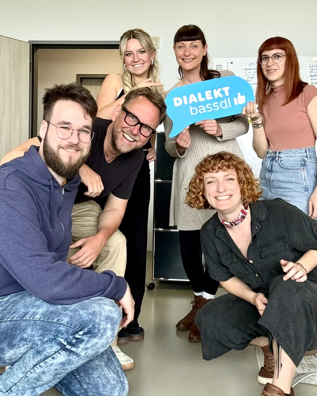 Das Team der machen.de Medien und Marketing GmbH, eine Person hält ein Schild mit der Aufschrift Dialekt bassd