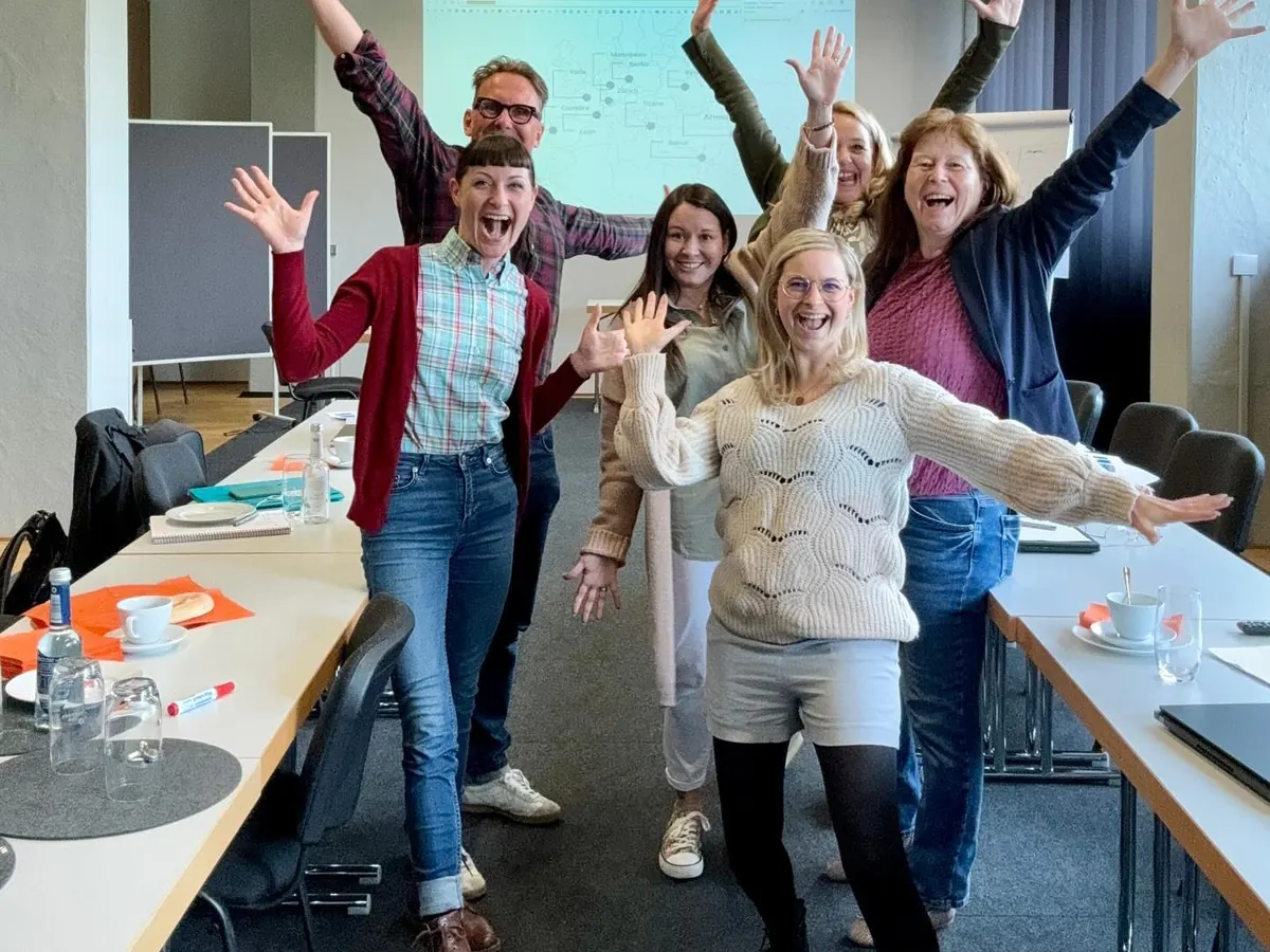 Workshop-Teilnehmerinnen und -Teilnehmer jubeln am Konferenztisch